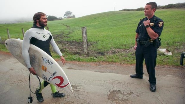 Surfer Joao Demacedo walks past a San Mateo County Sheriff's deputy along a private road to Martin's Beach, a popular surfing and fishing spot, in Half Moon Bay, Calif.