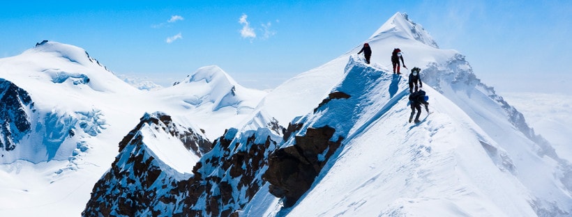 Mountaineers make their way across a snowy ridge.