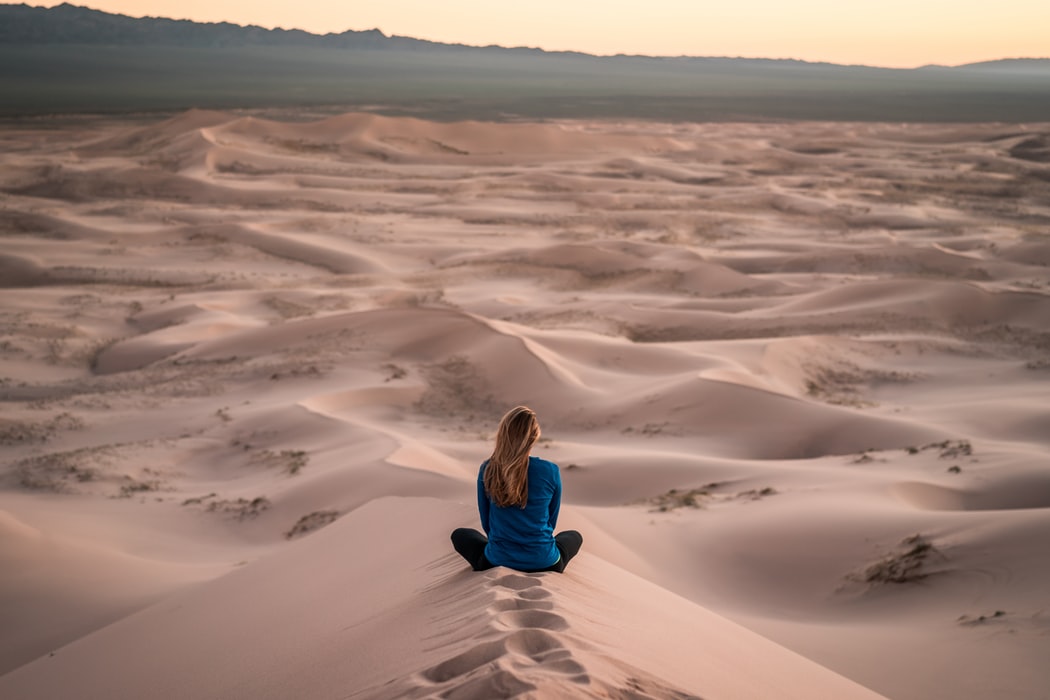 Woman achieves mindfulness practicing meditation on some amazing dunes.