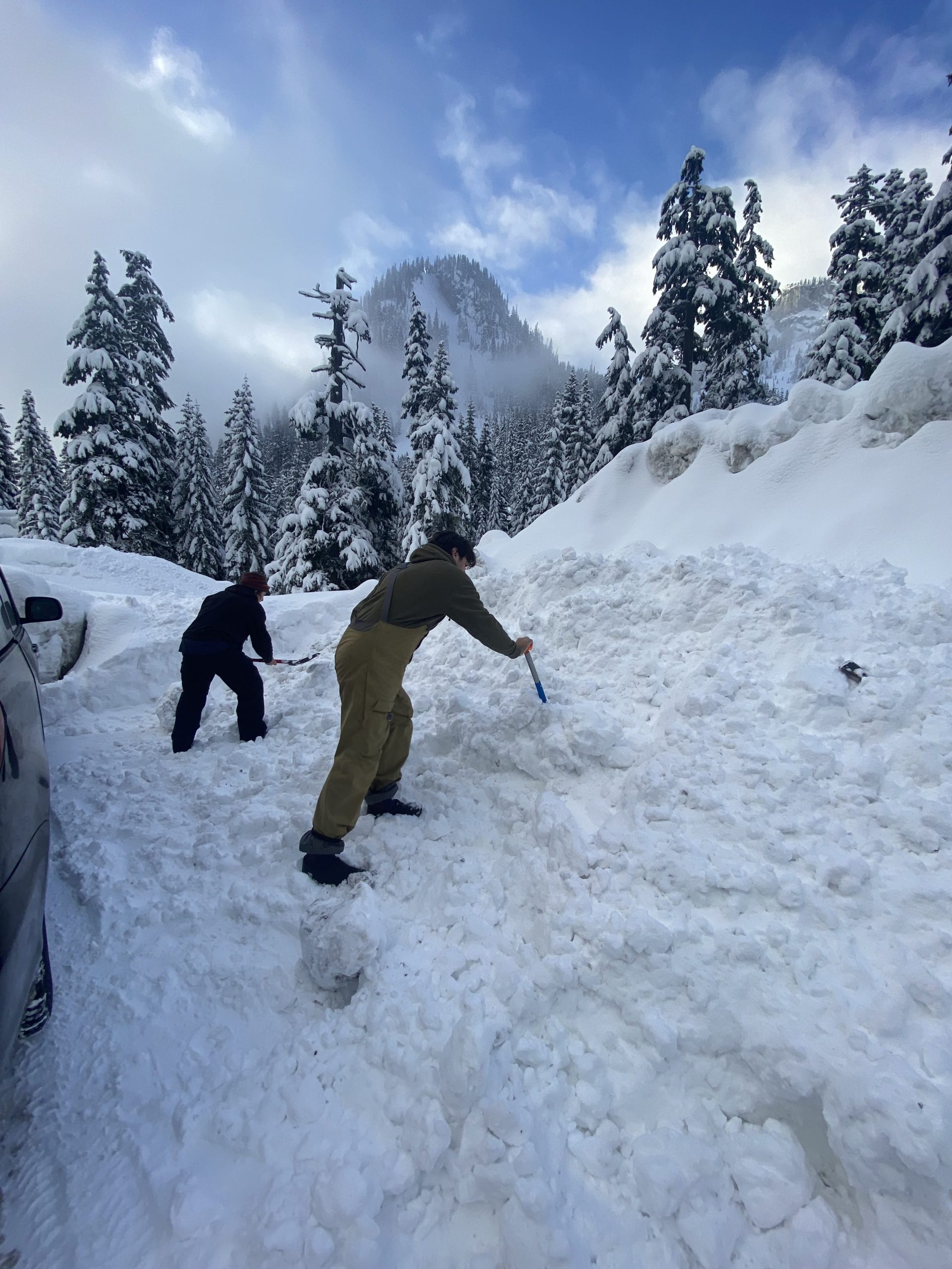 Two people digging snow out of a mound next to a parked car, Alpental, summit at Snoqualmie, Washington