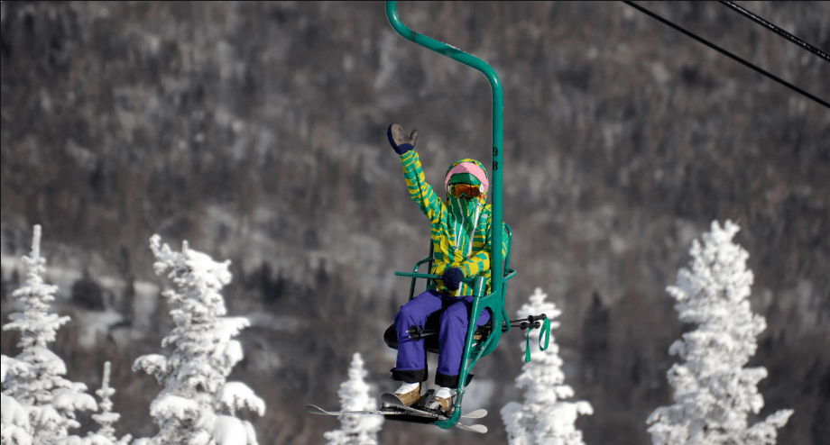 A happy skier waves to the camera as they ride up the iconic Mad River Glen single chair.