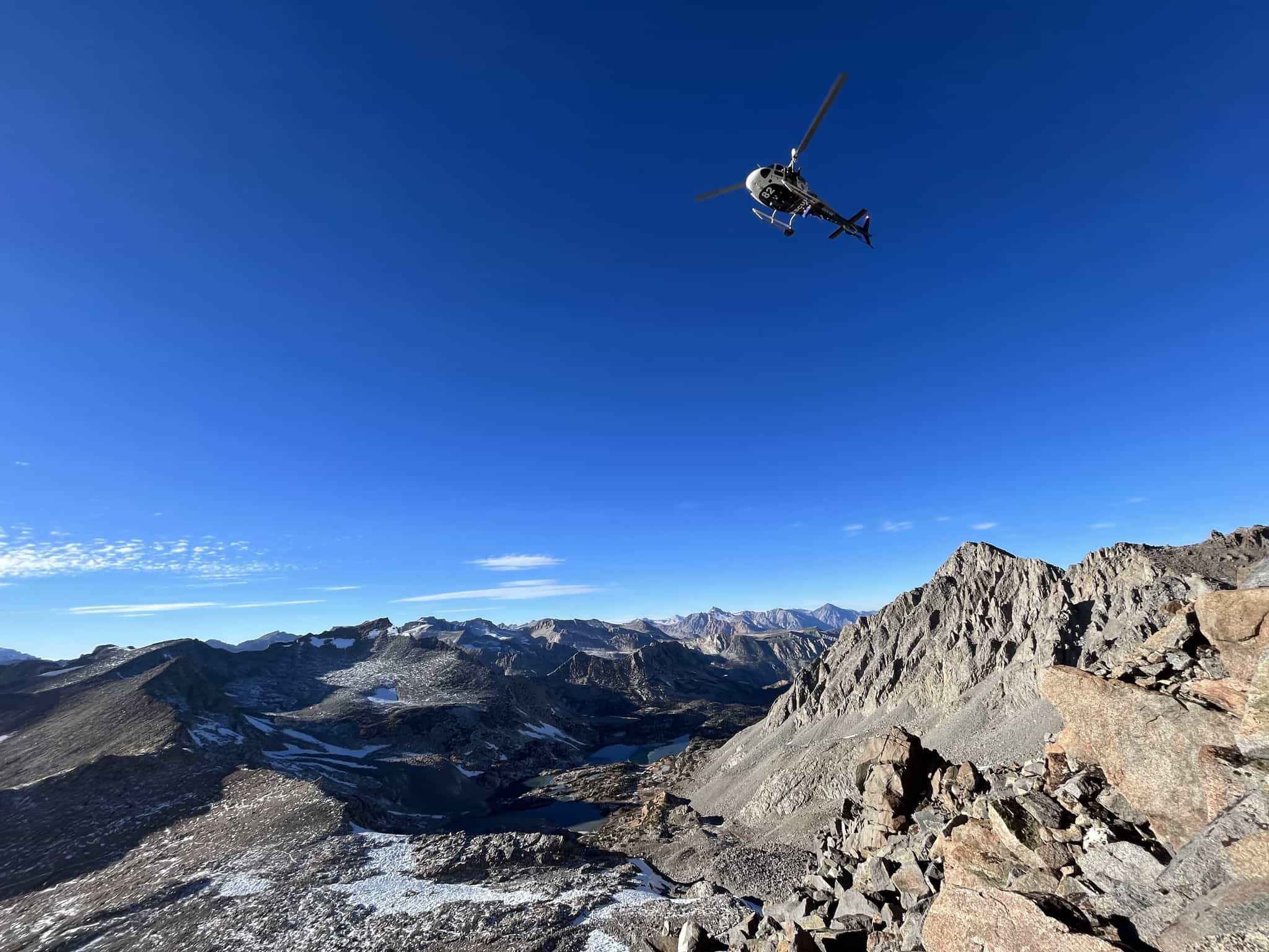 helicopter searching mountain terrain for overdue climber in bright blue sky