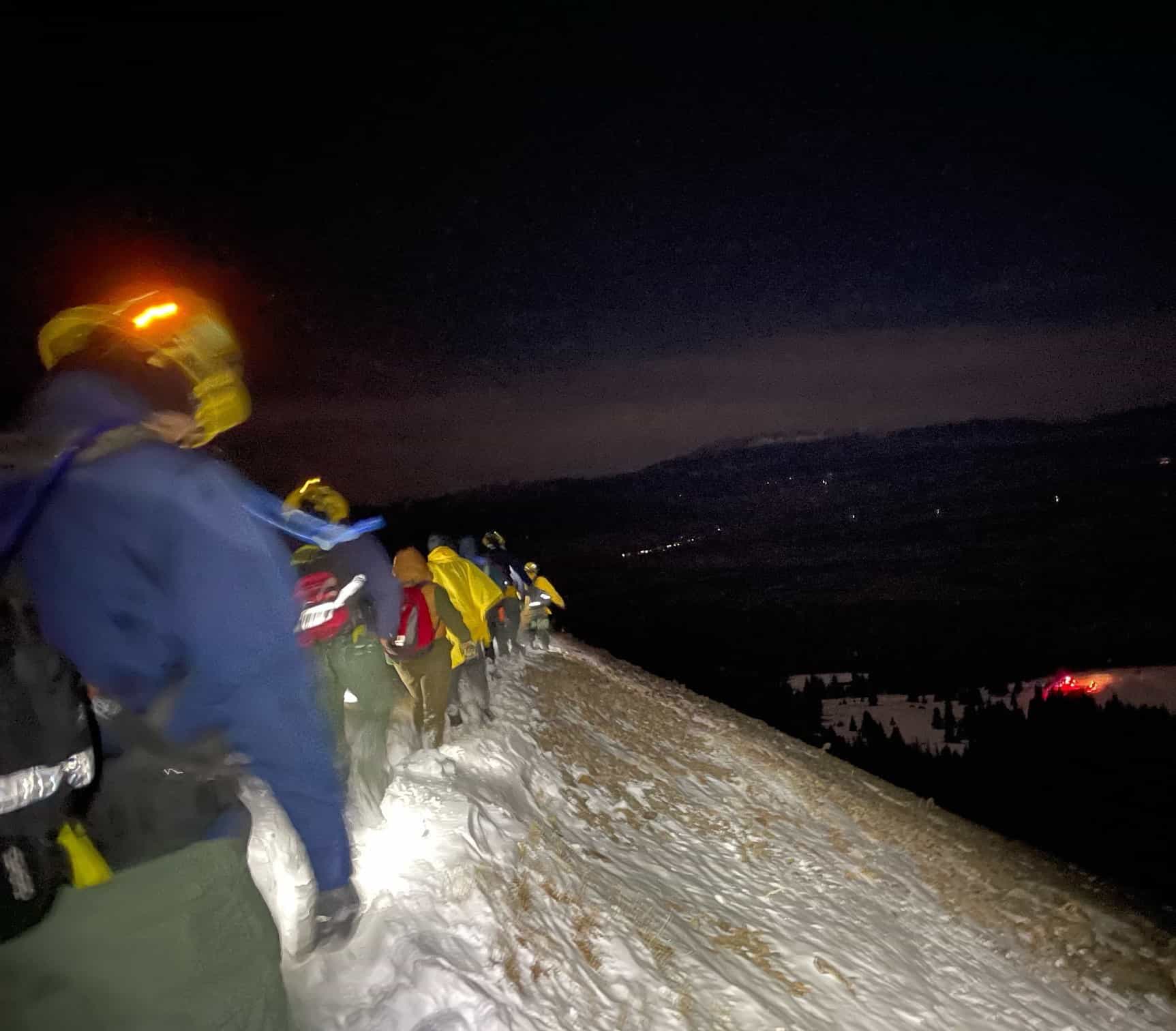 rescuers on dark snowy mountain trail with headlamps