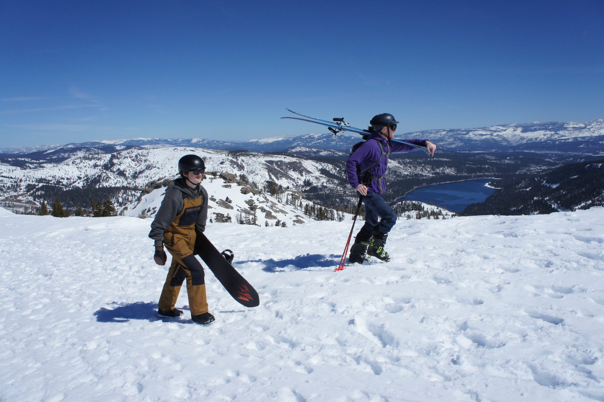 skier and snowboarder hiking up ridge at sugar bowl resort with donner lake in the background