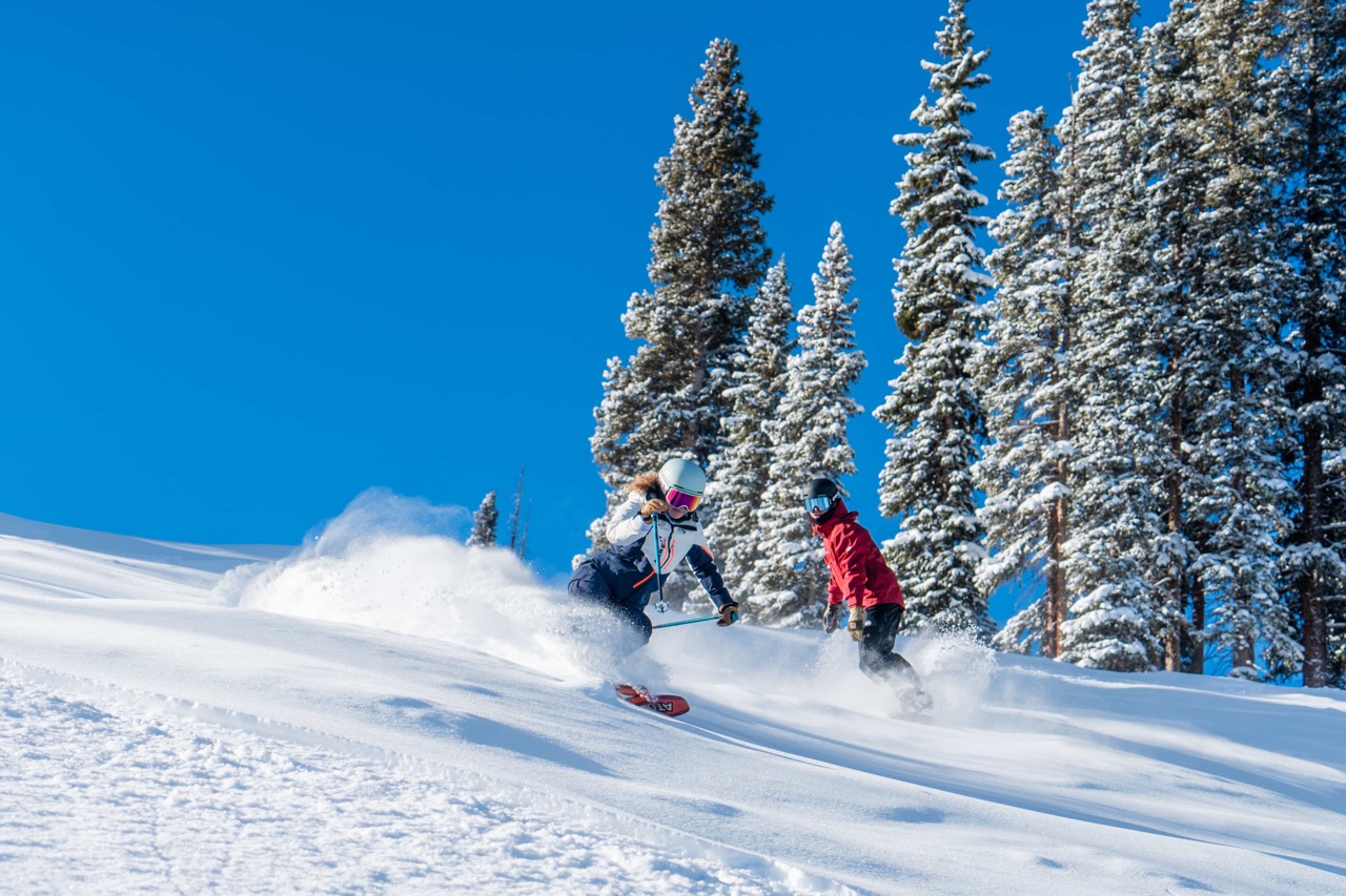skier and snowboarder in fresh snow with blue sky and green trees at copper mountain colorado