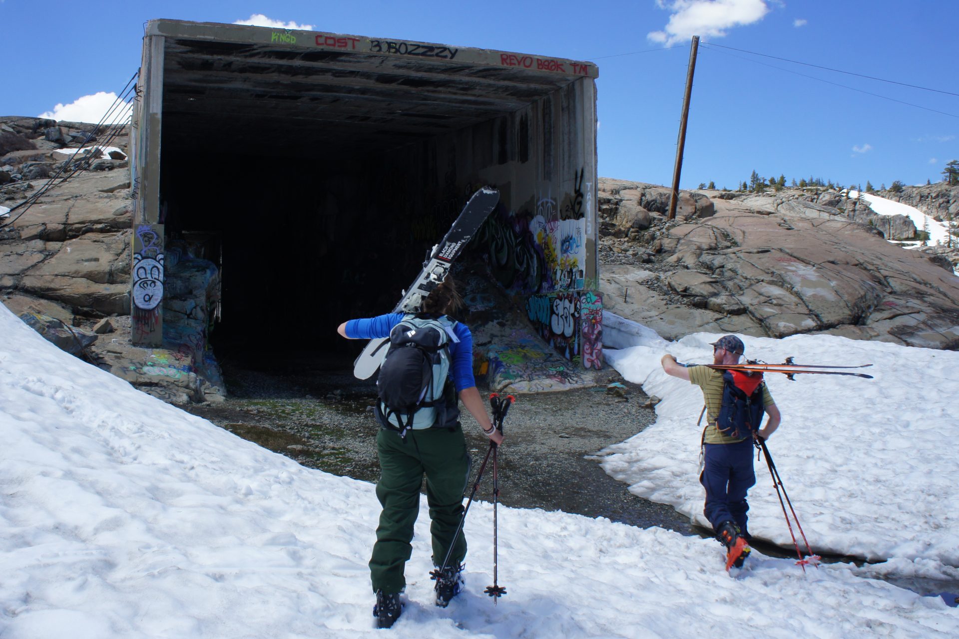 two skiers entering an old train tunnel covered in graffiti