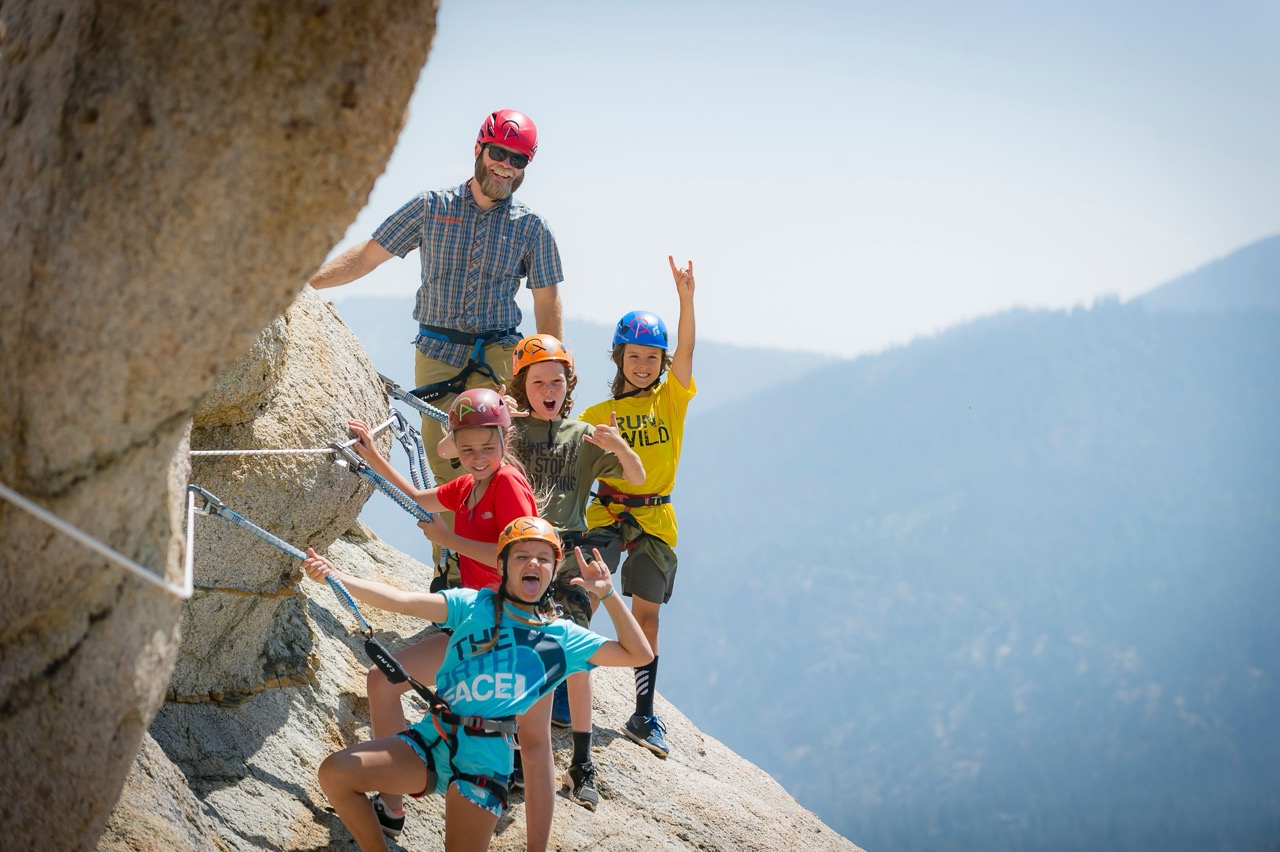 kids and an instructor on a rock face doing via ferrata at palisades tahoe in the summer