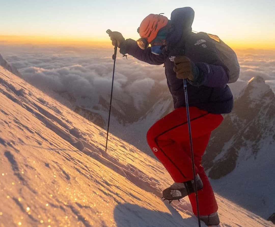 climber ascending snowy and icy K2 mountain with sunrise in the background