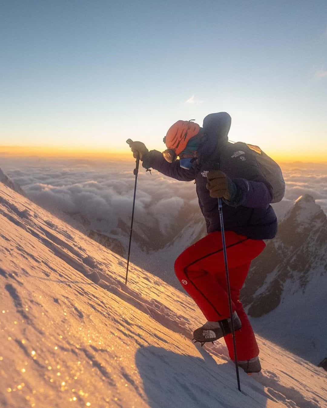 climber ascending snowy and icy K2 mountain with sunrise in the background