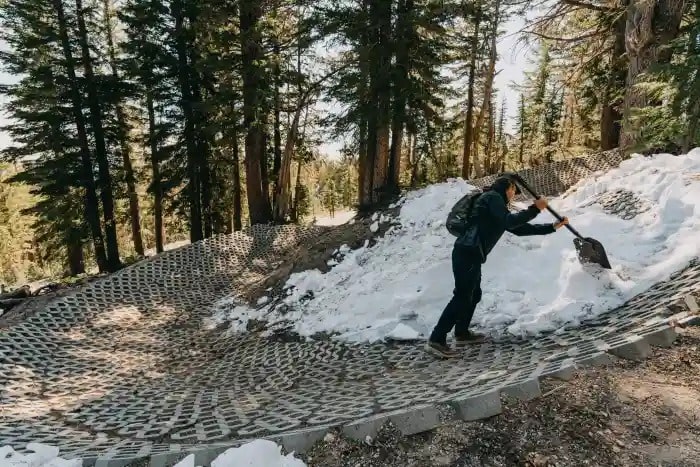 A person shoveling snow off a mountain bike trail