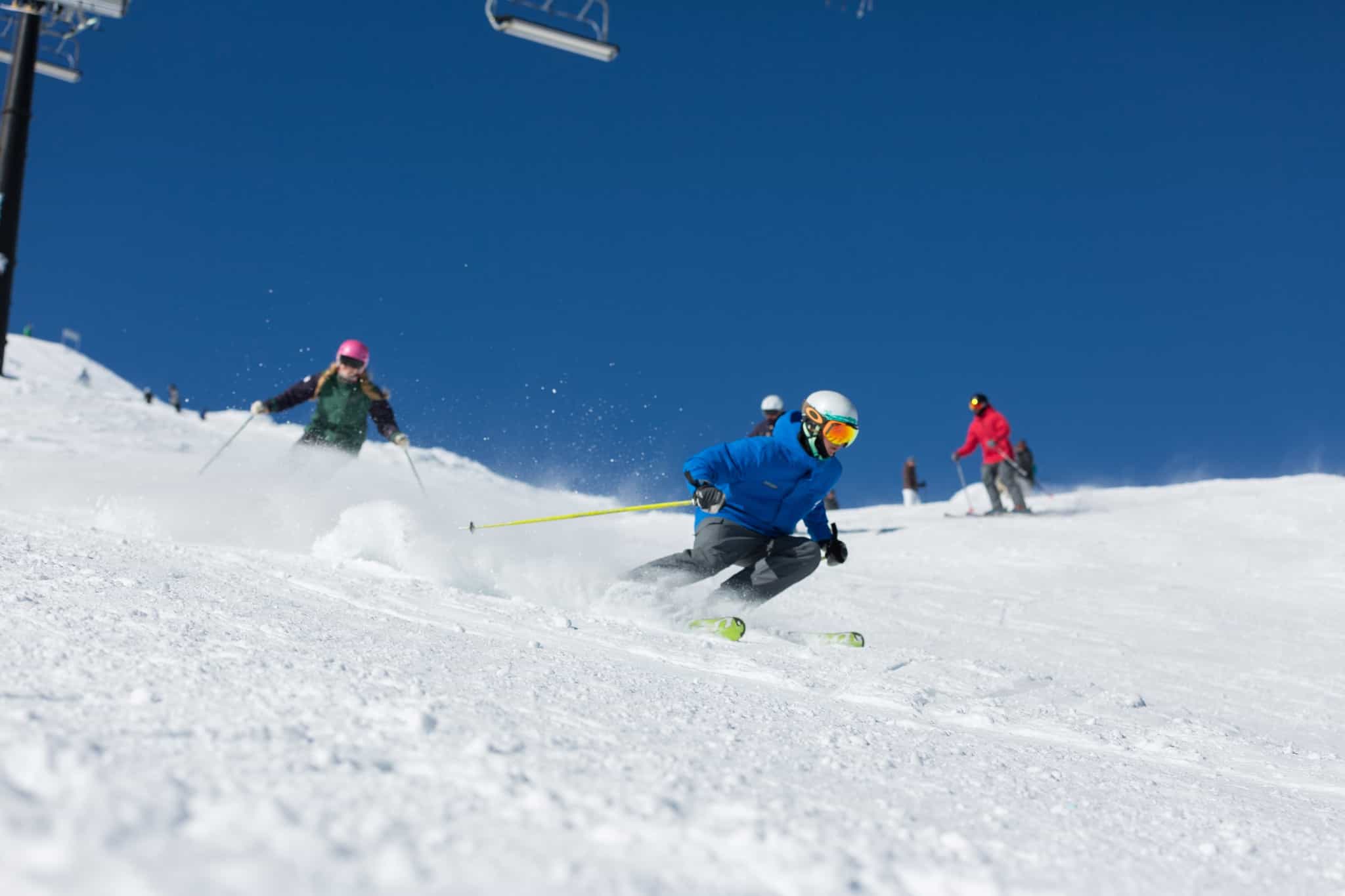 Skiers shredding on snowy slope in fron of blue skies at Turoa, New Zealand