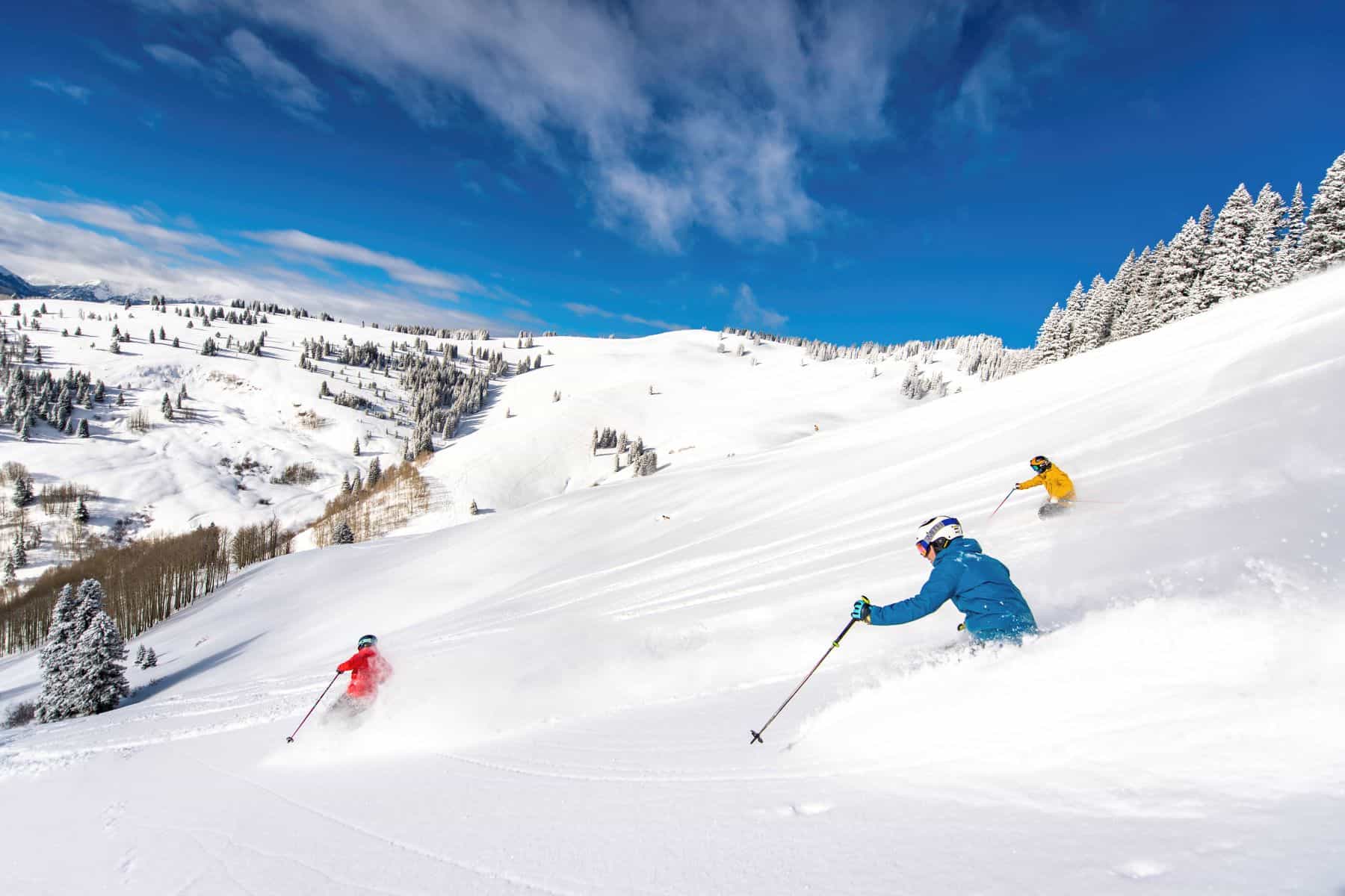 skiers in deep powder on snowy mountain with blue sky