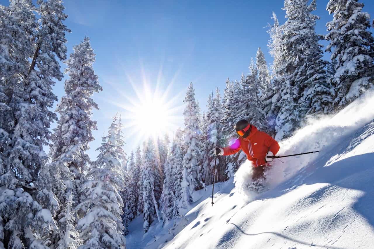 skier in deep powder in front of sunshine and blue skies on snow Vail Mountain