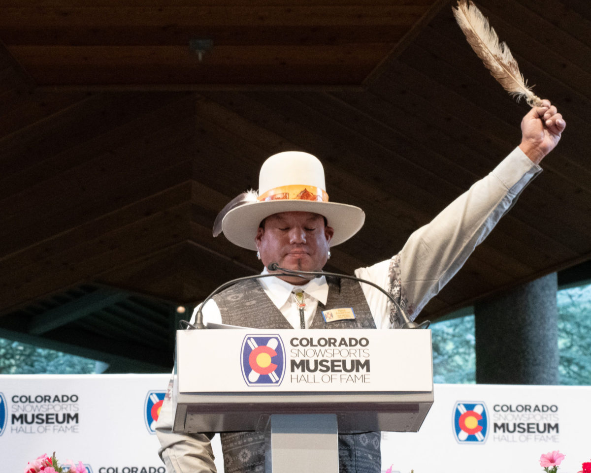 Ross Anderson stands at the podium proudly accepting his award with a feather in his hand.