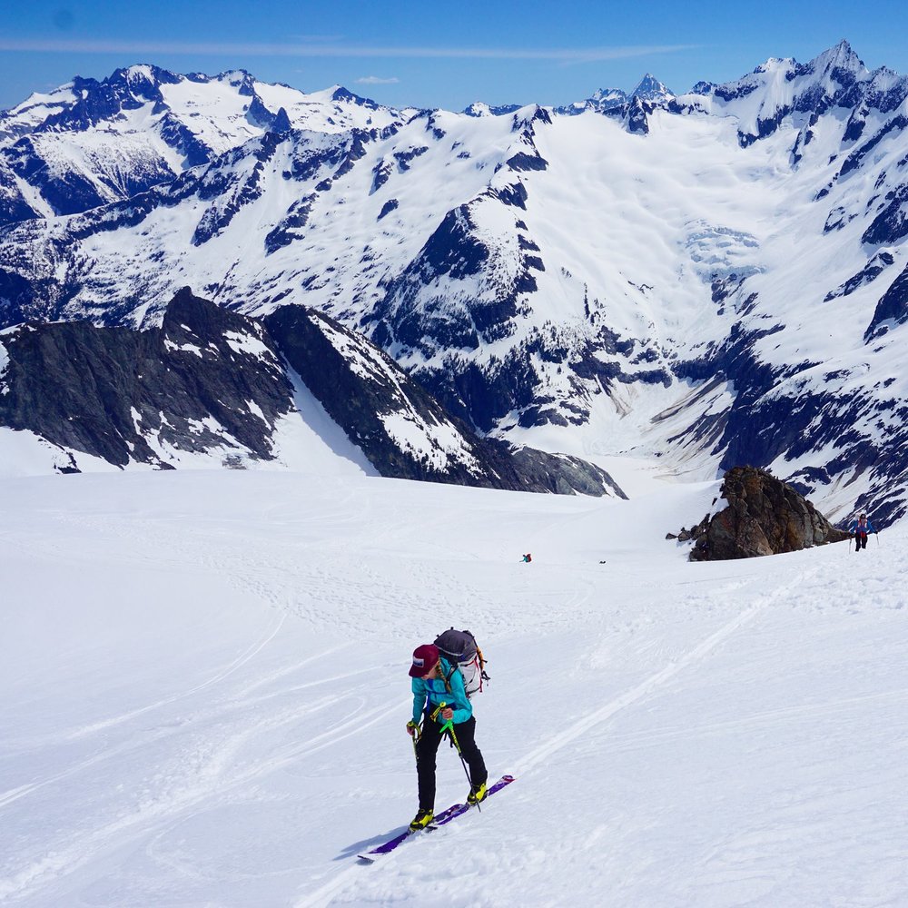 woman skiing up a snowfield with north cascades in the background