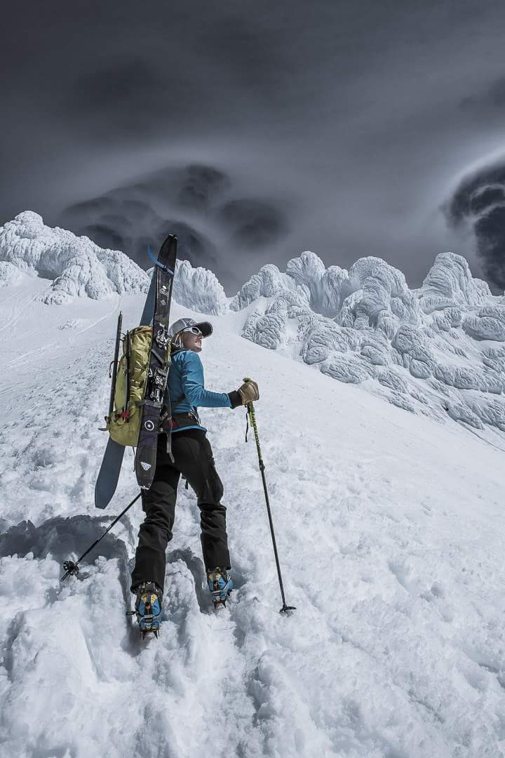 climber with skis on back ascending into steep icy terrain