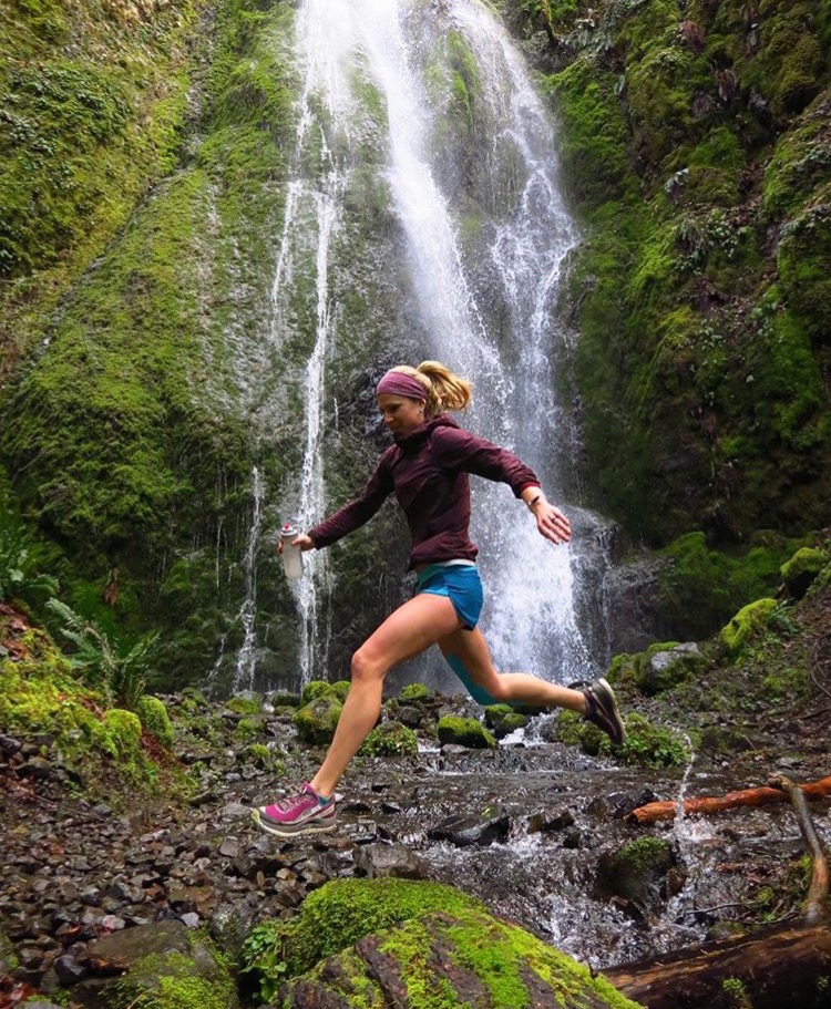 runner jumping over a stream in front of a small water fall