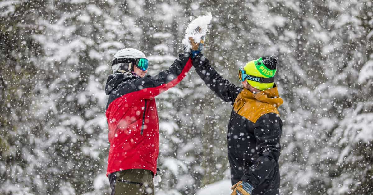 two skier and snowboarders giving a high five in the snow at mount hood meadows opening day