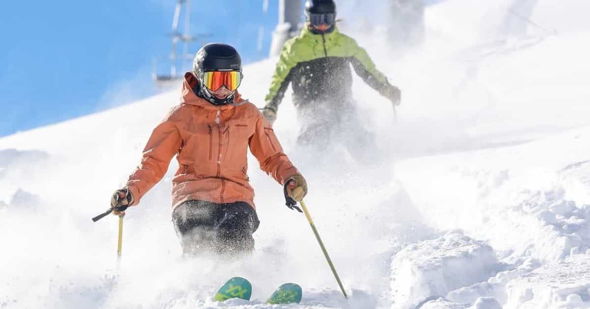 2 skiers in deep snow beneath chairlift and blue sky