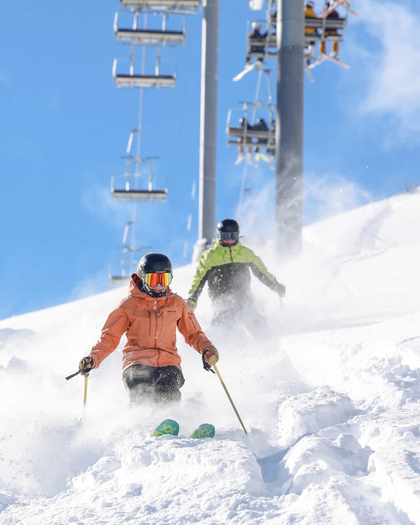 2 skiers in deep snow beneath chairlift and blue sky