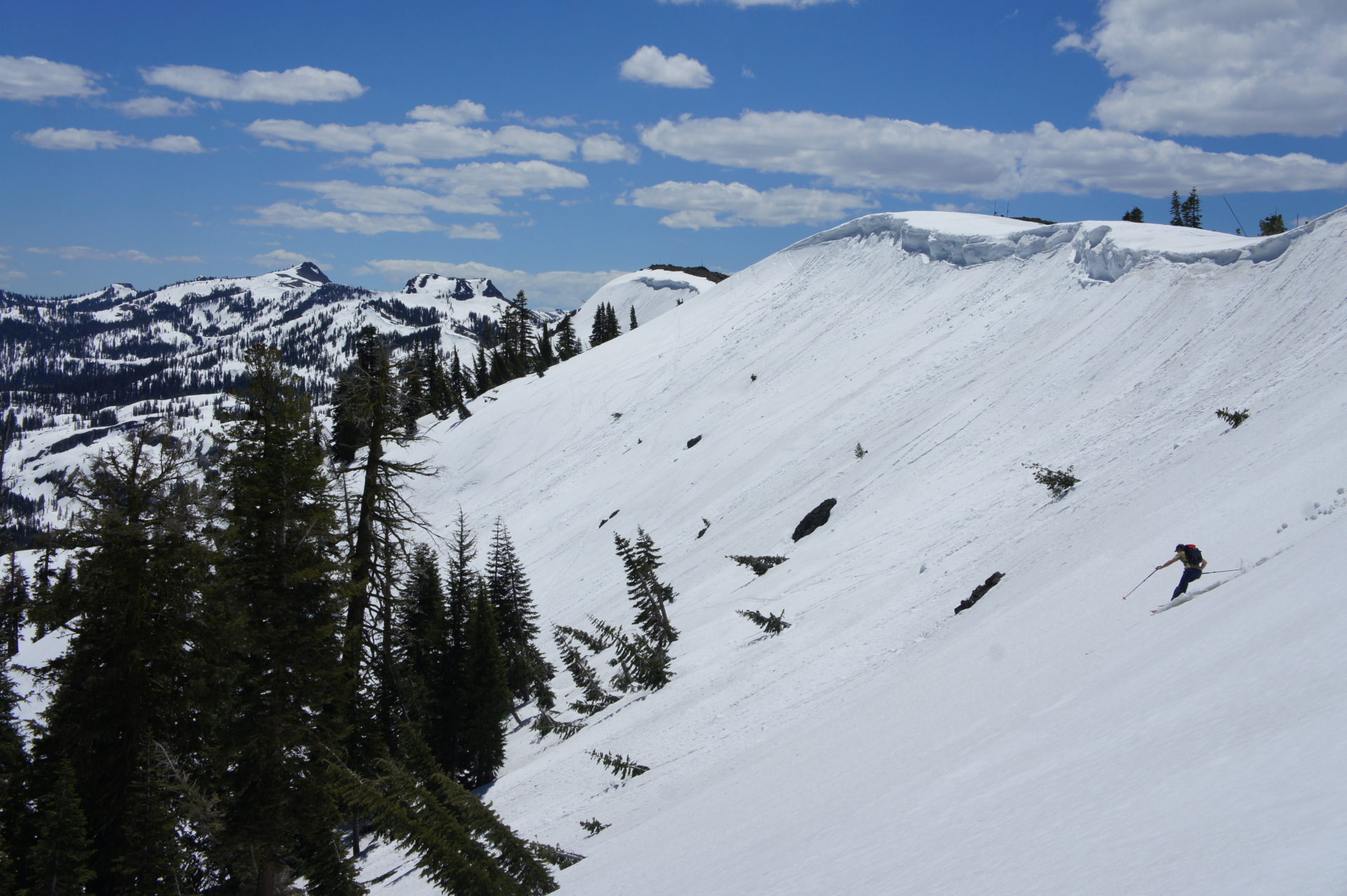 backcountry skier dropping into large bowl on a sunny day