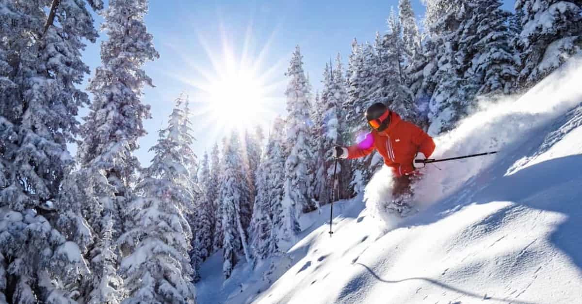 skier in deep powder in front of sunshine and blue skies on snow Vail Mountain