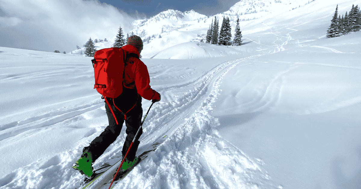 skier going uphill on snowy slope with red backpack