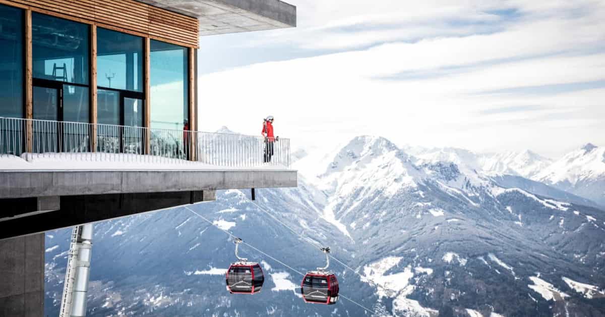 skier standing on the edge of a high balcony overlooking a gondola and snowy mountain peaks