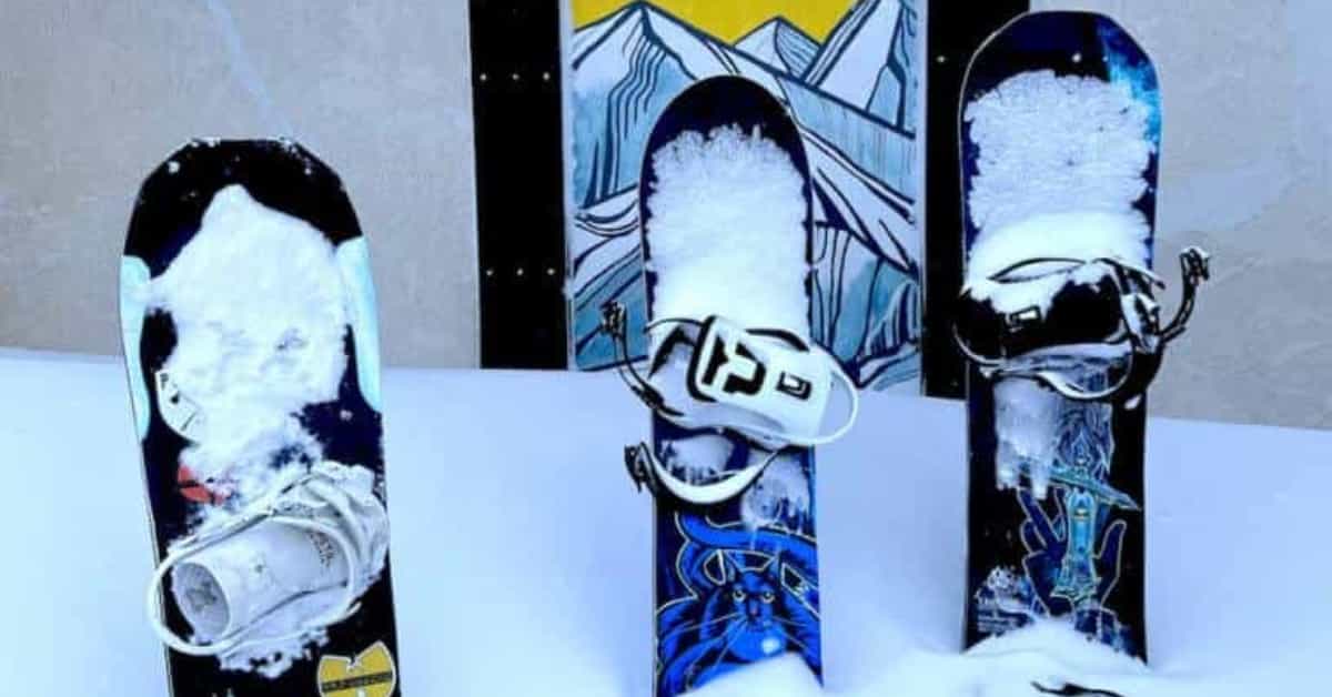 3 snowboards stood up in snow infront of an art picture